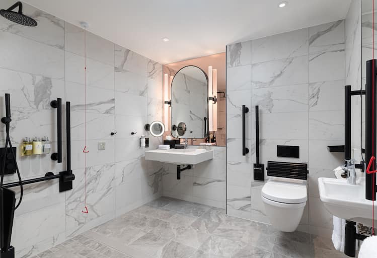 A modern, luxurious accessible bathroom in white,  with matt black accessories, grab rail, safety hinged support rail  