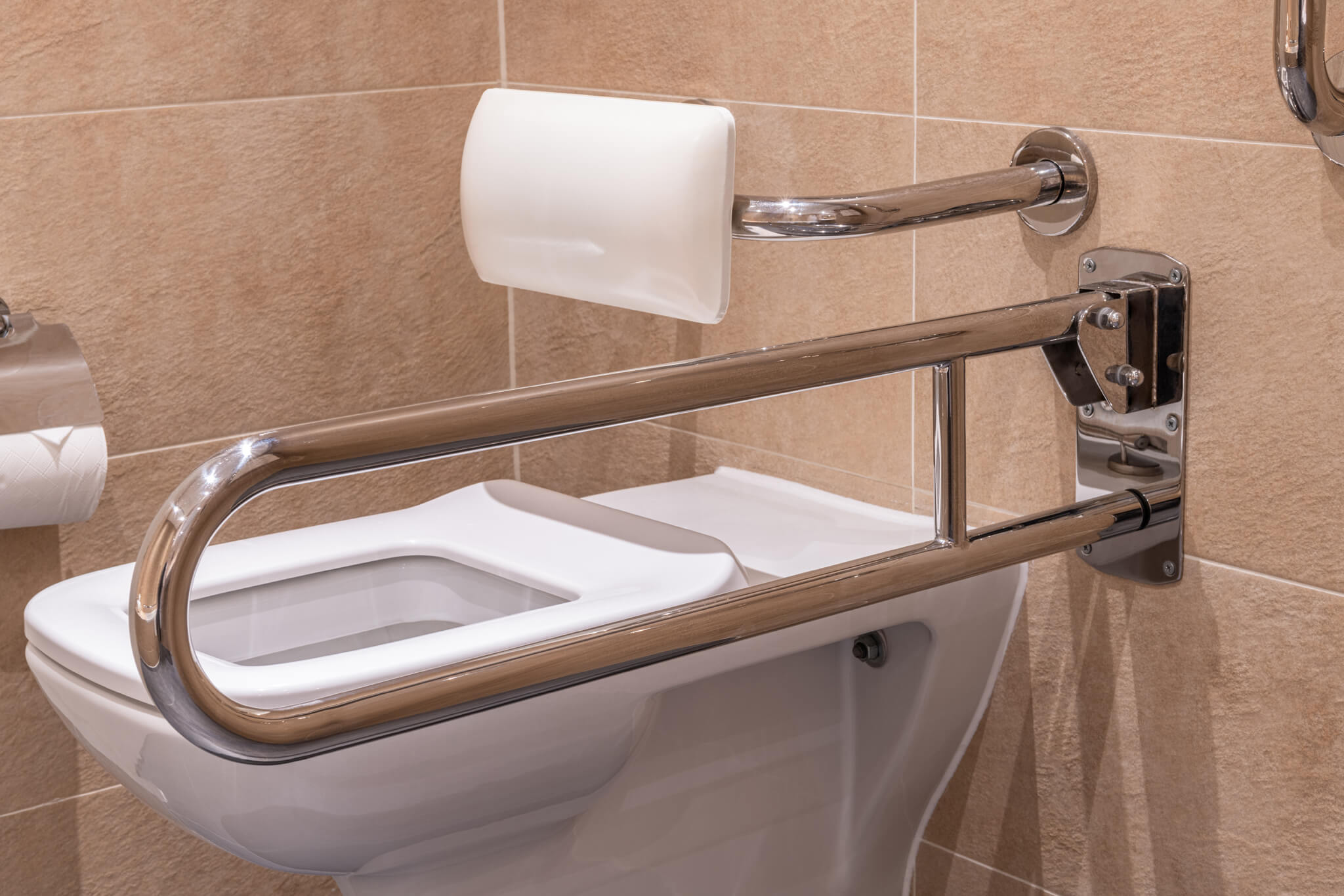 A close up of a hingled support rail and white back rest above the toilet. Both in stainless steel