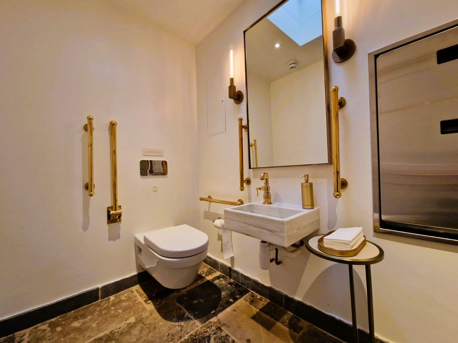 A toilet and basin with luxurious, solid brass accessible bathroom items like grab rails, removable hinged rail and gold taps